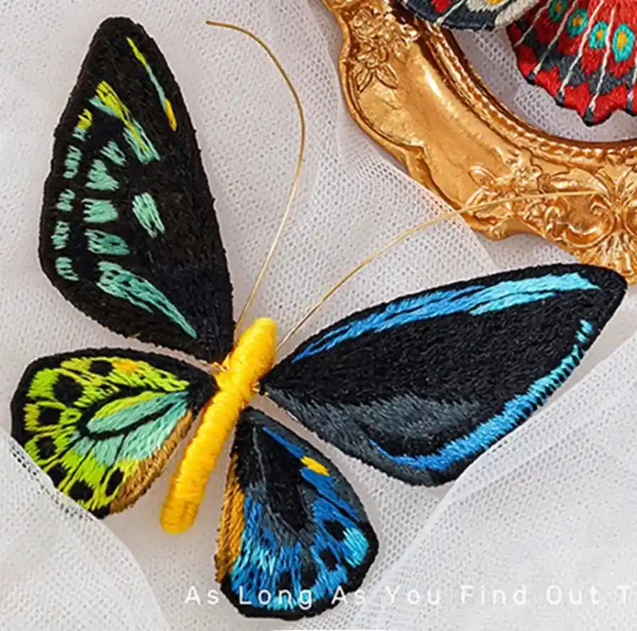 A close-up of a colorful, hand-embroidered butterfly with black wings featuring blue, green, and yellow patterns, resting on…