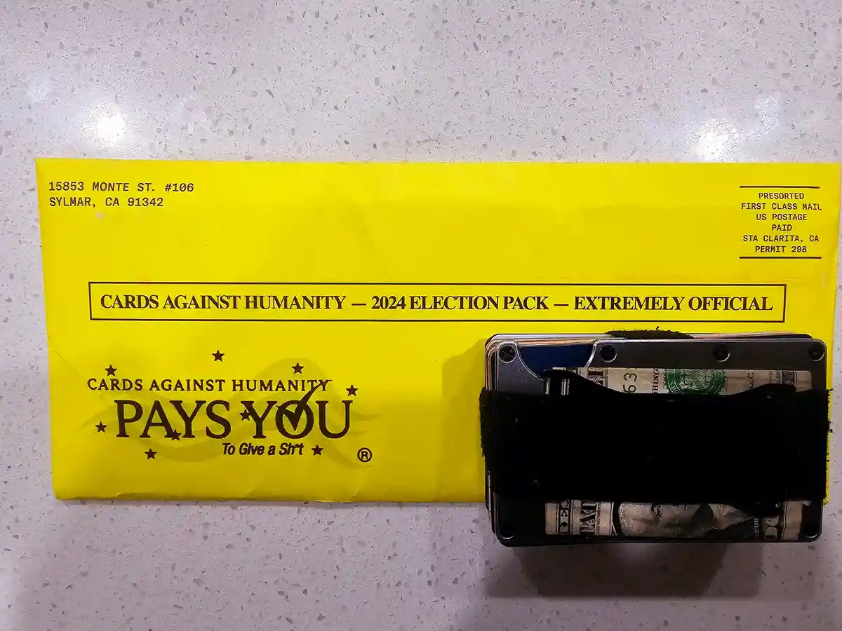 A bright yellow envelope labeled 'CARDS AGAINST HUMANITY — 2024 ELECTION PACK — EXTREMELY OFFICIAL' and 'CARDS AGAINST…