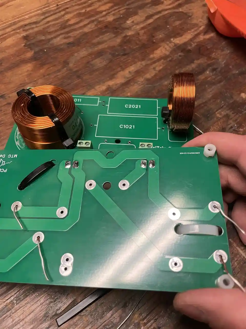 A hand holds a green circuit board with visible solder points and copper traces, showing the underside where components are…