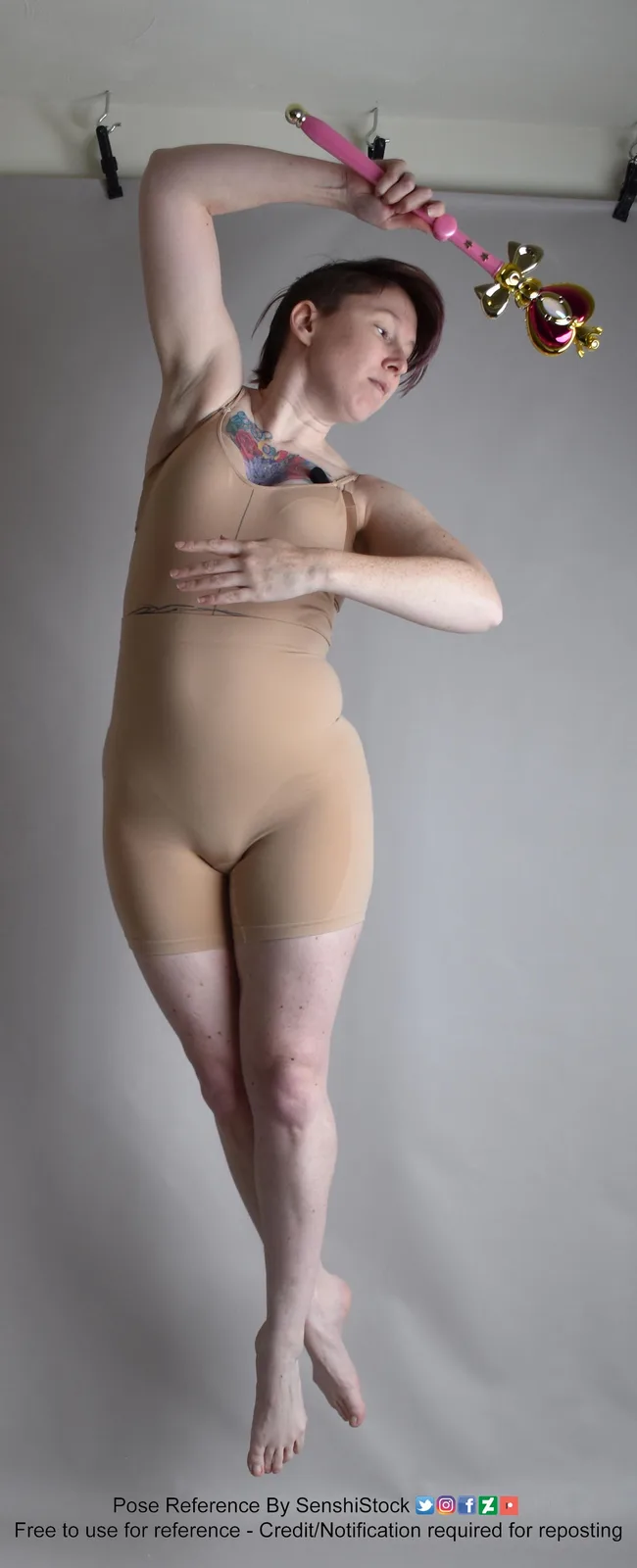 A person with short hair and a visible tattoo on their neck is wearing a beige bodysuit and holding a pink and gold magical…