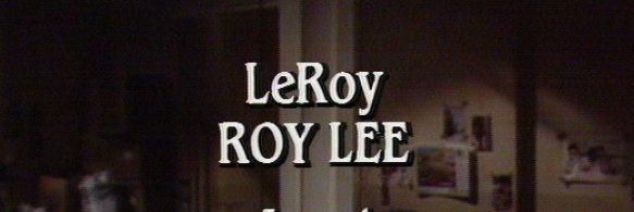 A dimly lit indoor scene, likely from a TV show, with white text overlaid that reads 'LeRoy ROY LEE'. The text is in a bold…