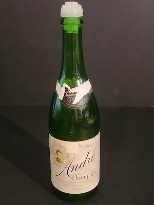 A green glass champagne bottle with a white foil cap and a label reading 'André Champagne' is shown against a dark…