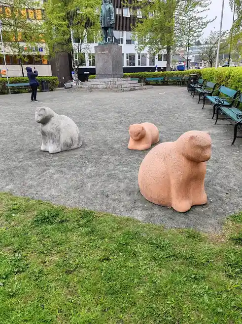 Three large, stylized stone sculptures of polar bears sit in a public plaza, two in reddish-brown stone and one in gray. In…