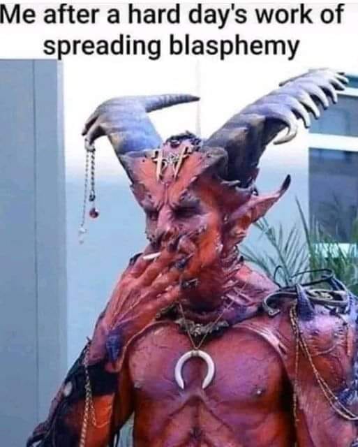 A person in elaborate demonic costume with horns, a crescent moon necklace, and chains, holding a cigarette to their lips…
