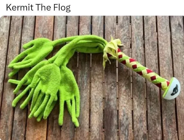 A bright green plush toy resembling Kermit the Frog, but shaped like a flog or whip with multiple hand-like flaps, lies on a…