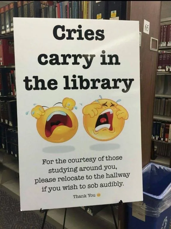 A white sign in a library setting displays the text 'Cries carry in the library' above two large crying emoji faces. Below…