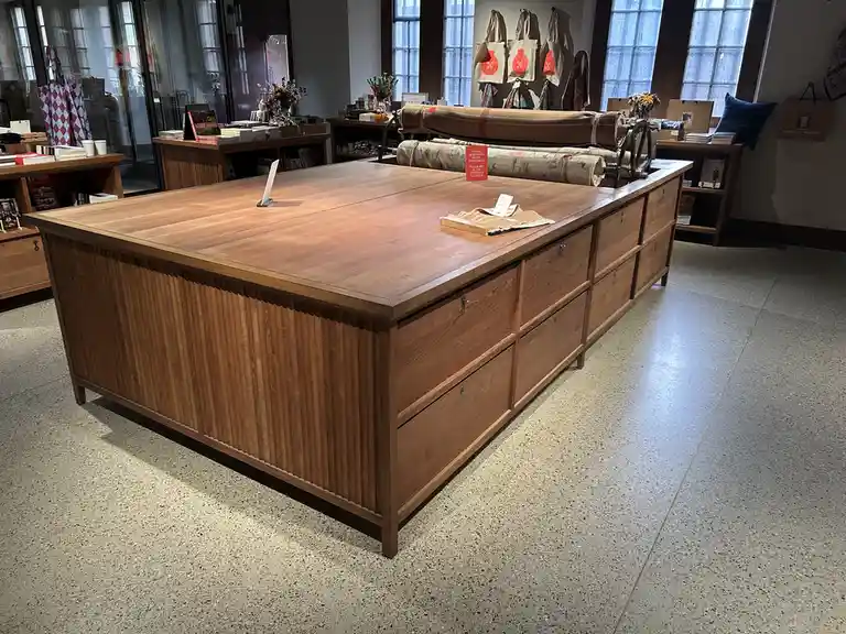 A large, wooden, multi-drawer counter in a retail store, with a small red sign on top that reads 'PLEASE PAY AT THE ENTRANCE…