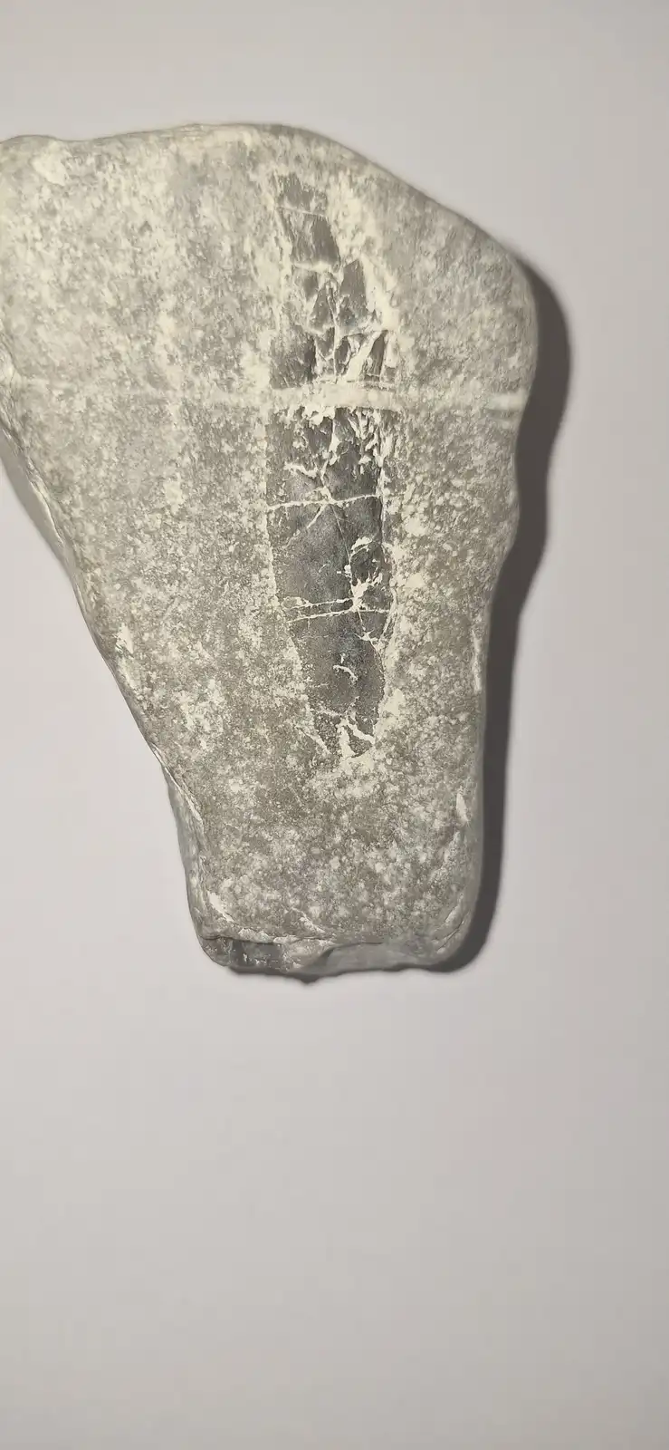 a close-up photograph of a gray, weathered stone axe head with a prominent vertical crack running down its center, set…