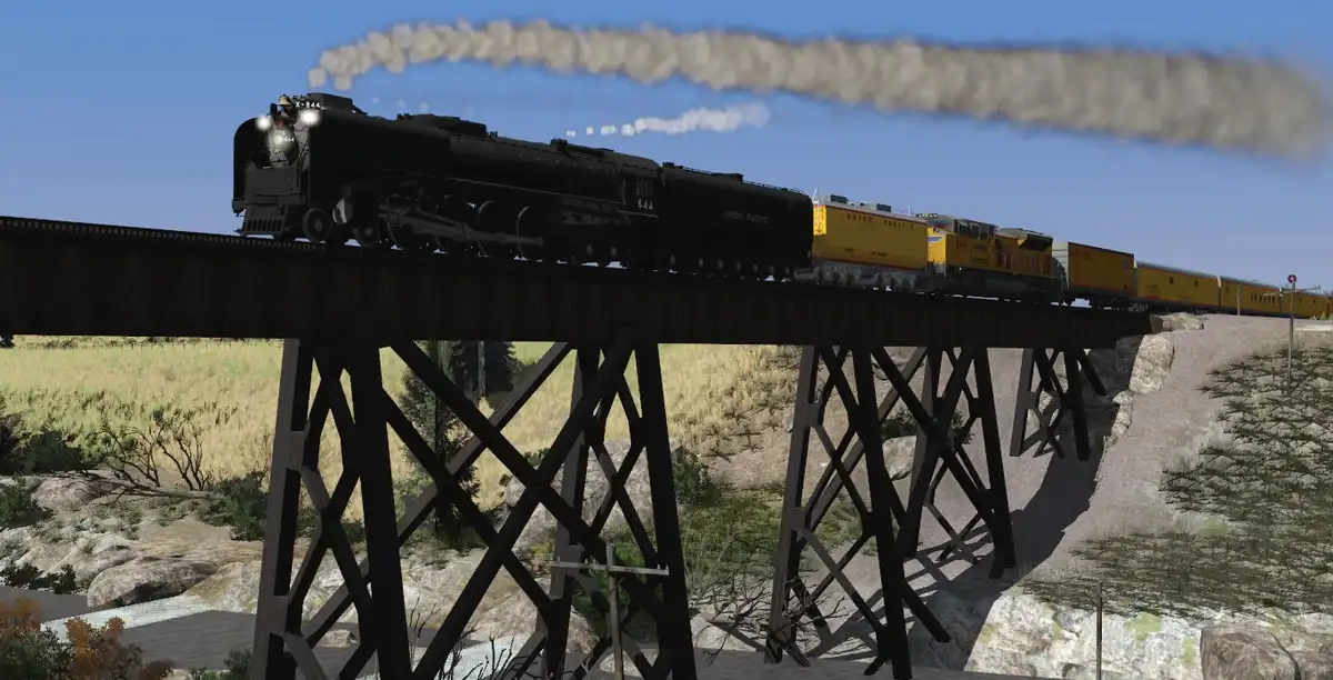 A black steam locomotive, Union Pacific 844, pulls a long train of yellow Union Pacific freight cars across a wooden trestle…