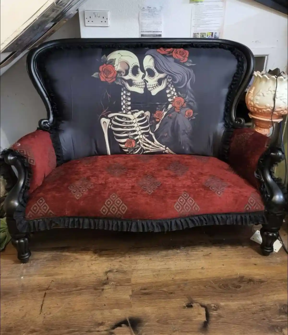 A vintage-style black-framed couch with red patterned upholstery and black ruffles, featuring a large graphic of two…