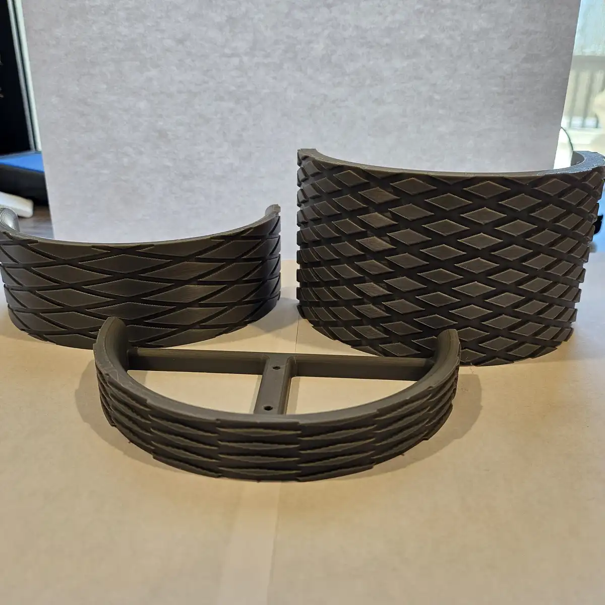 Three 3d-printed, curved, black plastic objects resembling tire treads are arranged on a light-colored surface. Two are…