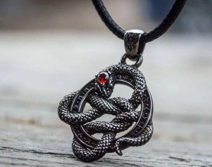 A close-up photo of a black metal pendant shaped like a coiled snake with a red gemstone for an eye, hanging from a black…