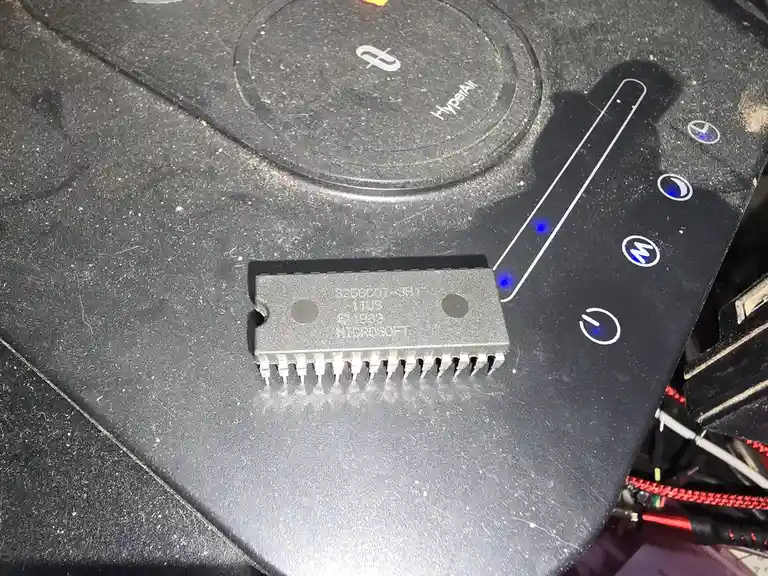 A close-up photo shows a physical integrated circuit chip labeled 'MICROSOFT' resting on a black computer case with glowing…