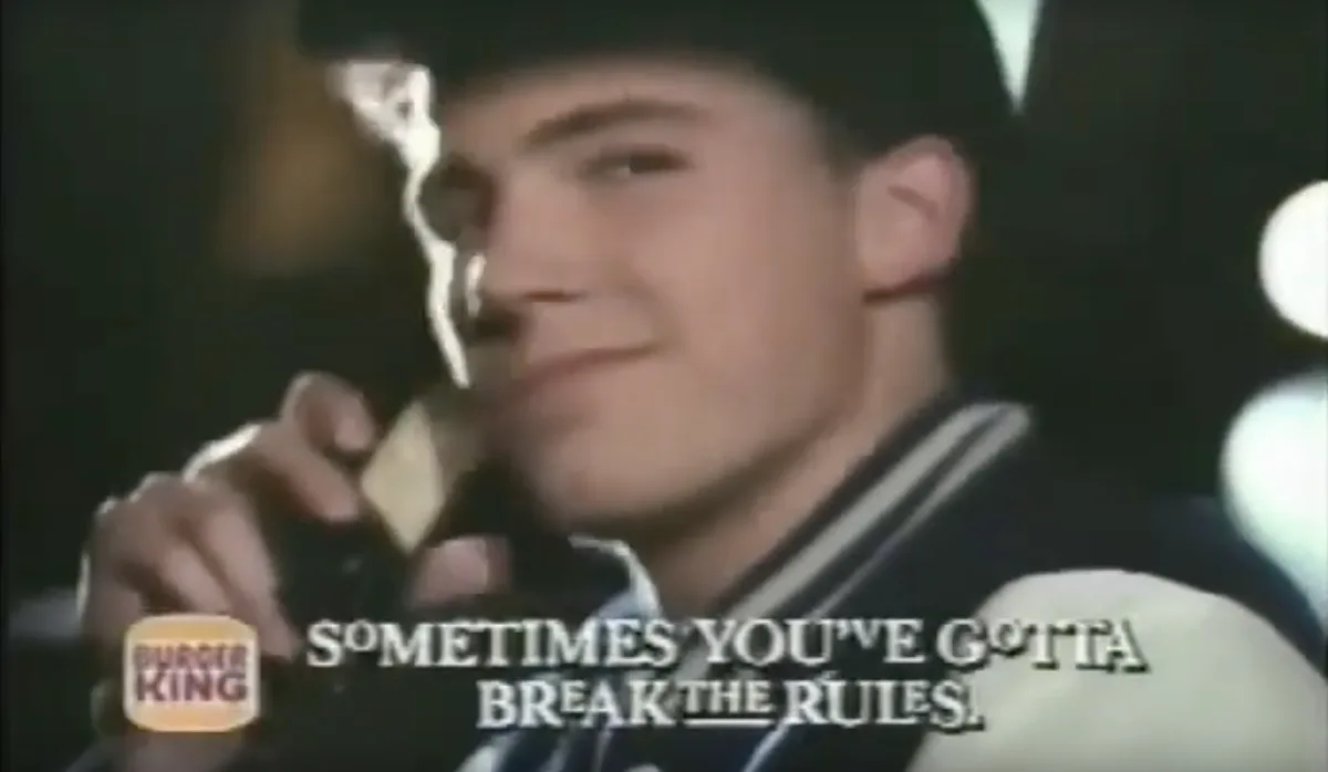 A young man in a varsity jacket and cap is shown eating a burger, with a Burger King logo in the corner. The overlaid text…