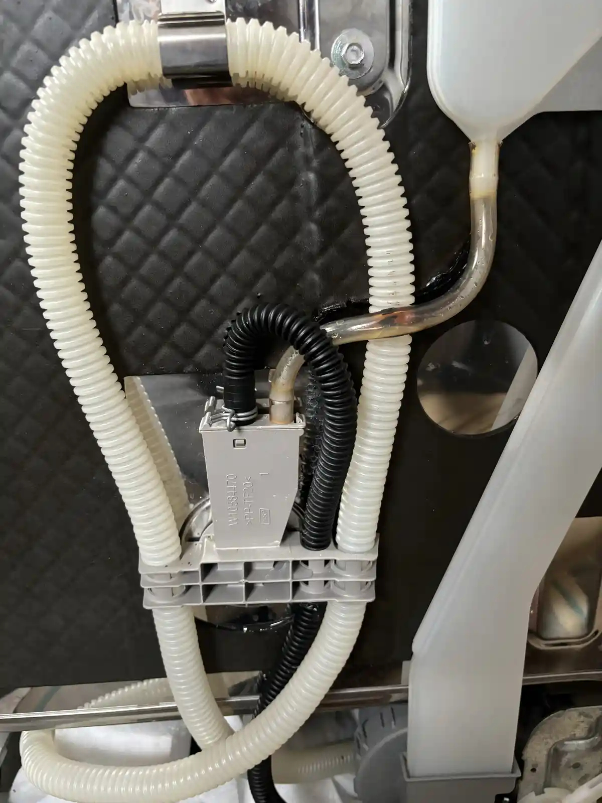 A close-up photo of a car's fuel system components, including corrugated white and black hoses connected to a gray…