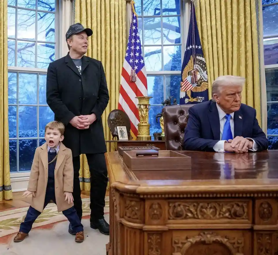 In the Oval Office, Elon Musk stands beside a small child in a tan coat who is yelling with an open mouth, while Donald…