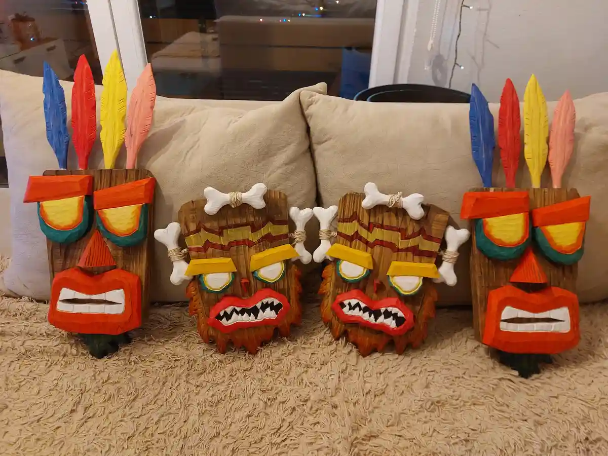 Four hand-carved wooden masks, resembling characters from the video game 'Crash Bandicoot', are arranged on a beige carpet…