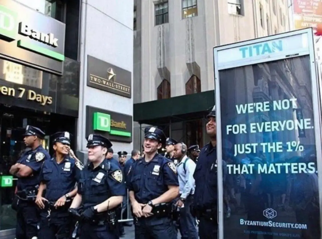 A group of police officers in uniform stand on a city street near TD Bank and Two Wall Street buildings, looking amused or…
