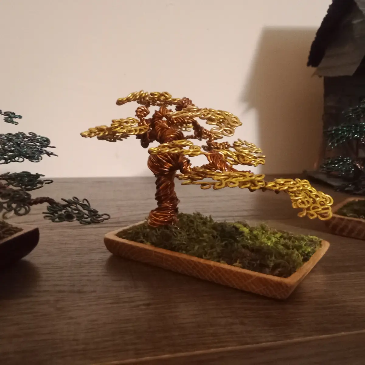 A close-up photo shows a decorative wire tree sculpture made of copper and gold-colored wire, shaped like a bonsai tree with…