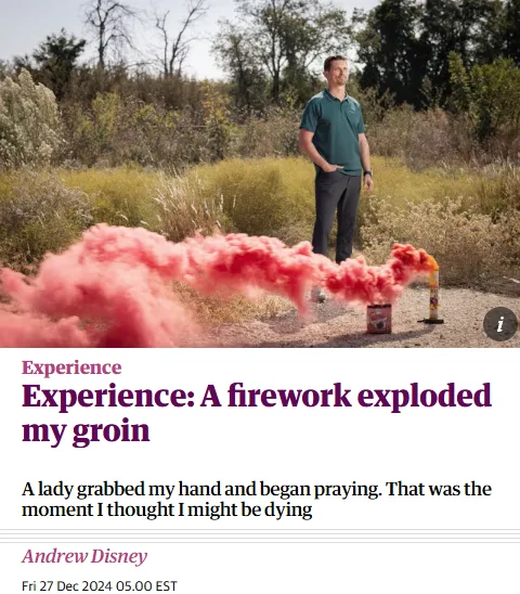 A man in a green polo shirt stands outdoors in a field with dry grass and trees, smiling while a red smoke bomb lies on the…