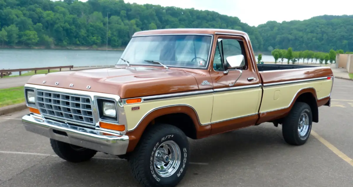 A vintage two-tone brown and cream Ford Ranger pickup truck is parked in a lot near a lake with a forested hillside in the…