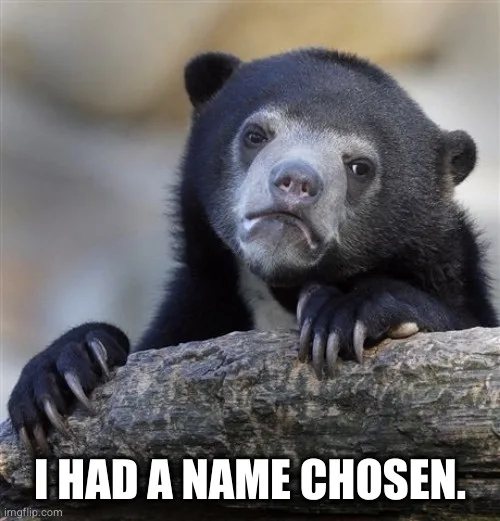 A close-up photo of a black bear with a sad, resigned expression, resting its paws on a log. The bear has dark fur, a…