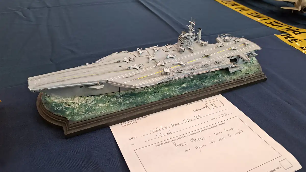 A detailed 1/700 scale model of the USS Harry S. Truman (CVN-75) is displayed on a green base, with a 'Model Entry Form' in…