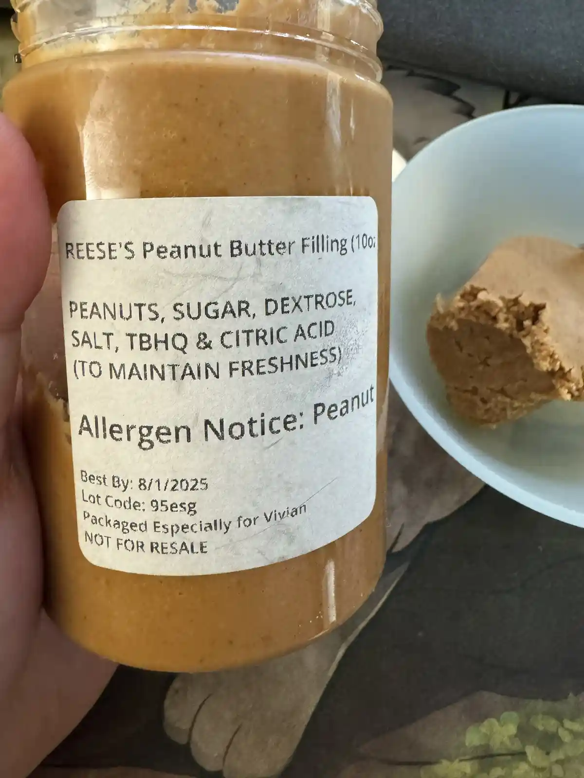 A close-up photo shows a hand holding a jar of Reese's Peanut Butter Filling, with its label clearly visible. The label…