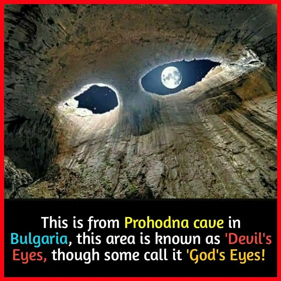 The image shows a natural rock formation with two large, eye-like holes carved into the cliff face. One hole contains a view…