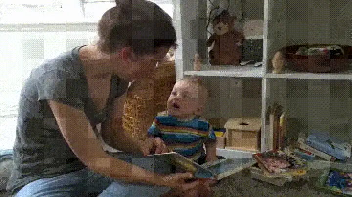 A woman sits on the floor reading a book to a baby. The baby initially looks engaged, then begins to cry and push the book…