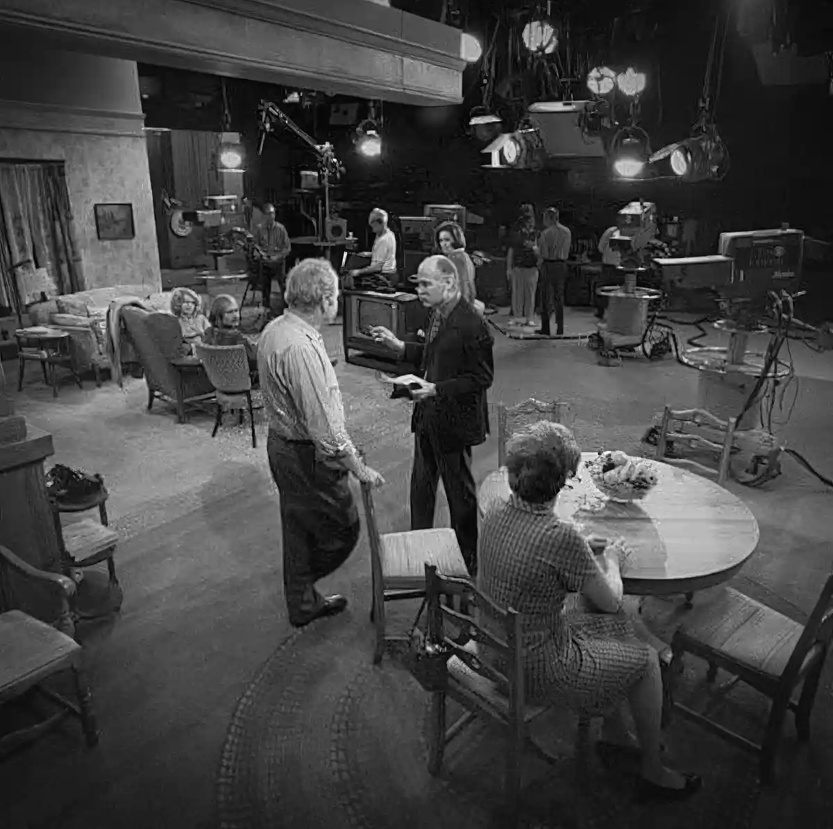 A black-and-white behind-the-scenes photo of the 'Bewitched' TV set, showing actors and crew in a studio with visible…