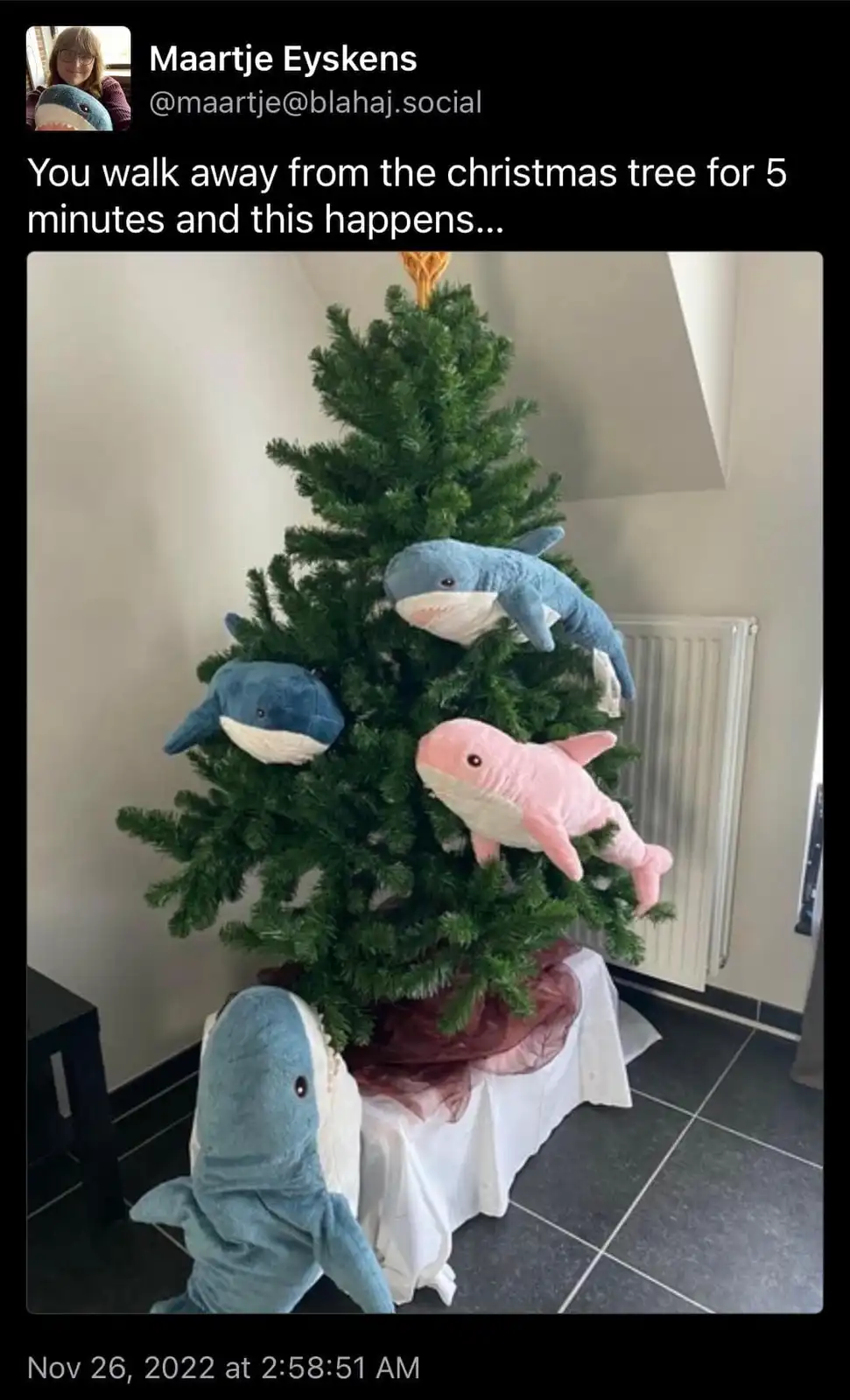 A christmas tree decorated with multiple plush sharks, including one large blue shark at the base and others perched on the…