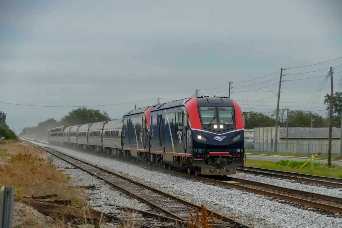 An Amtrak passenger train, numbered 309, travels along a set of tracks under an overcast sky. The locomotive is blue and red…