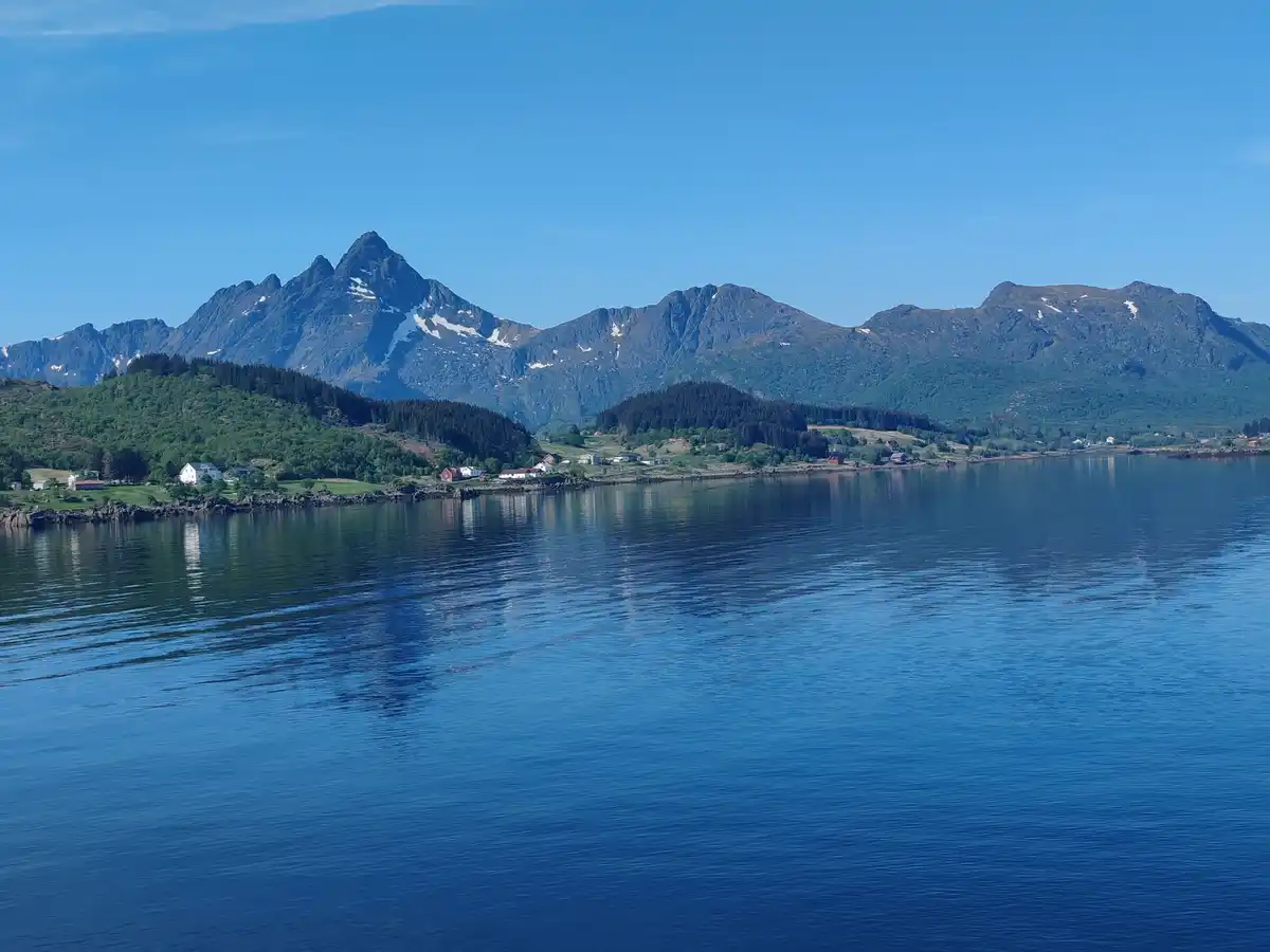 A scenic landscape photo shows a calm blue body of water in the foreground, with a shoreline featuring scattered houses and…