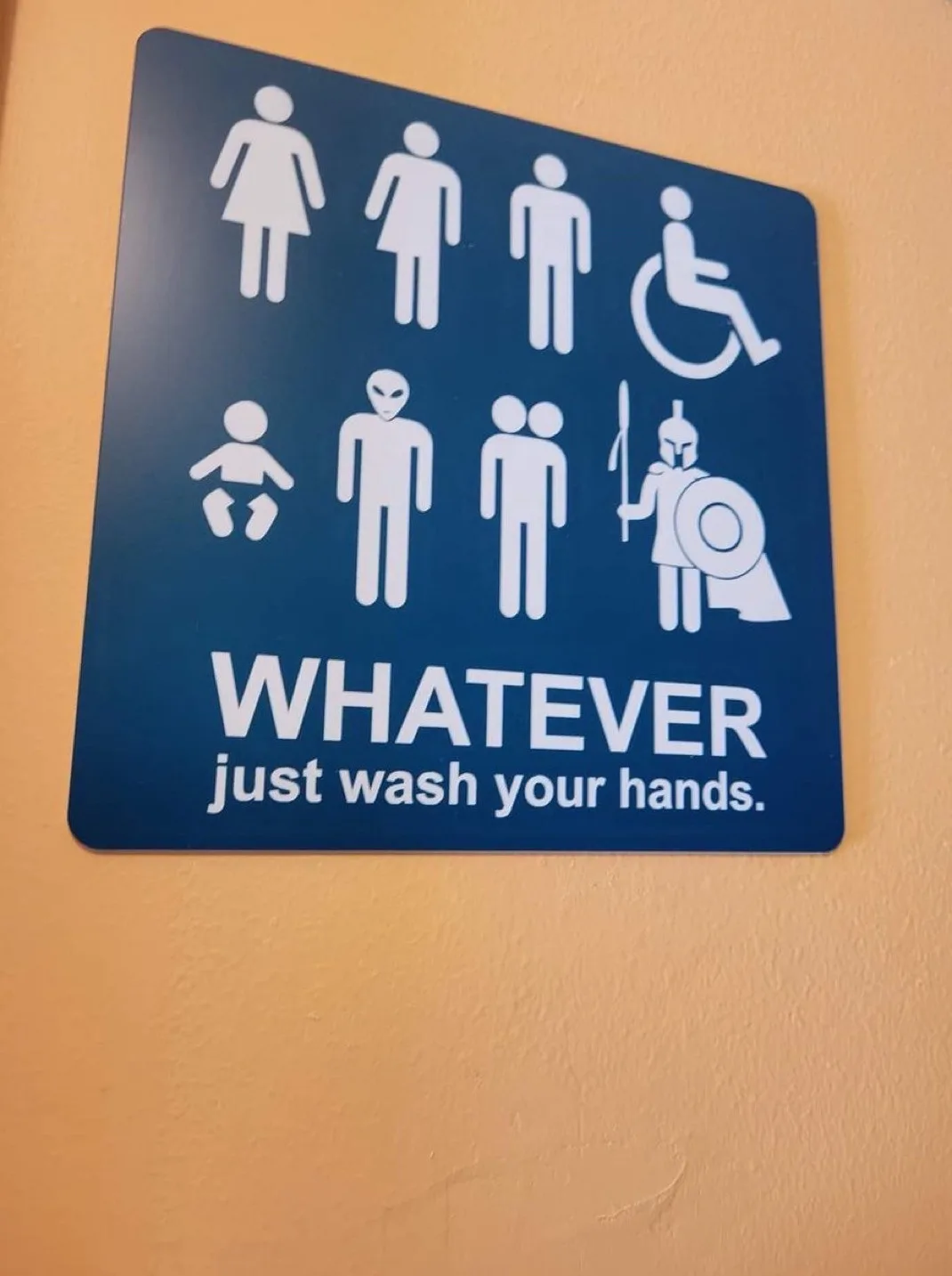 A blue restroom sign displays standard gender and accessibility icons, but replaces some with a baby, alien, couple, and…
