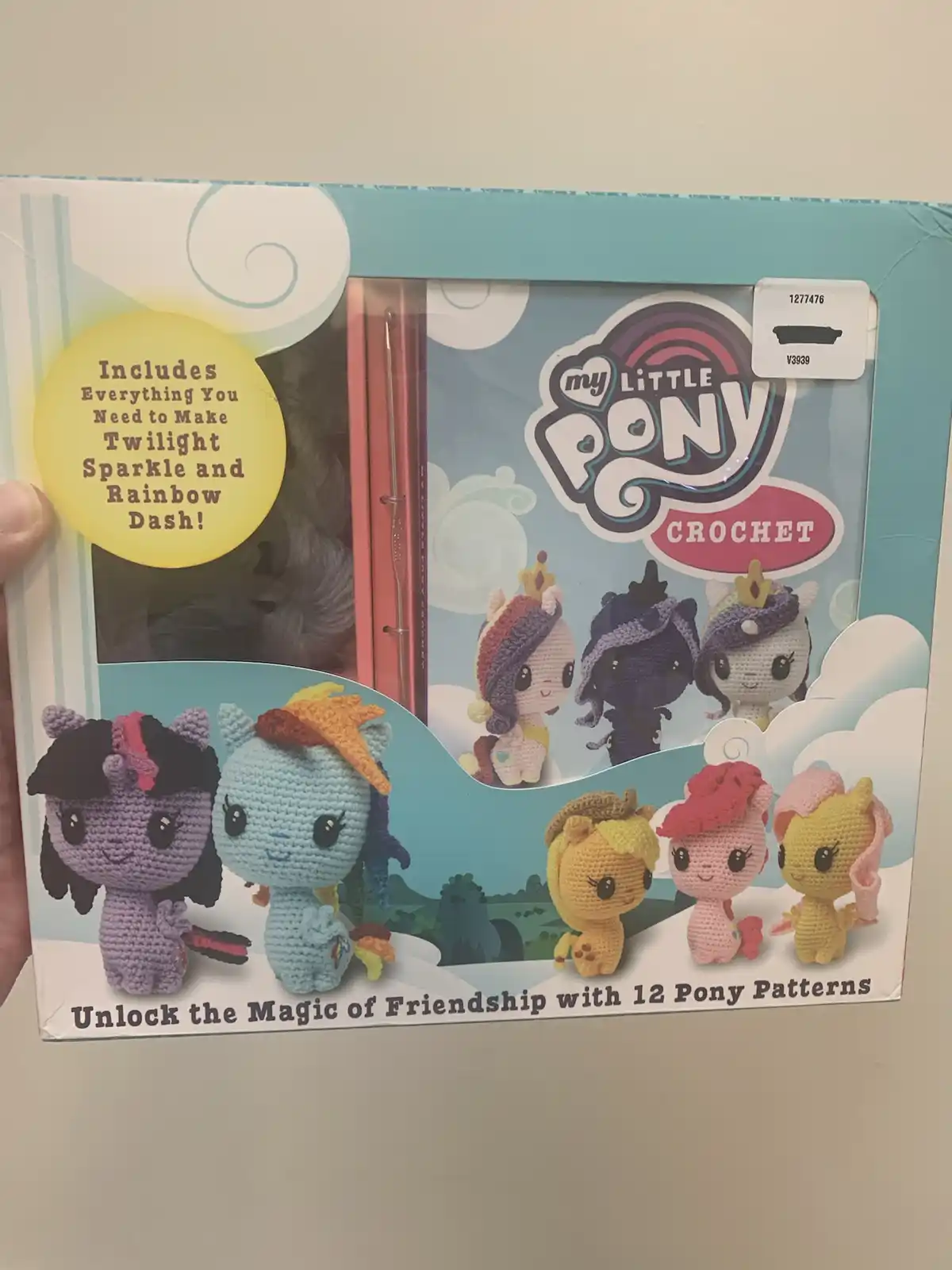 A hand holds a 'My Little Pony Crochet' craft kit box showing crocheted pony figures. The box art features several small…