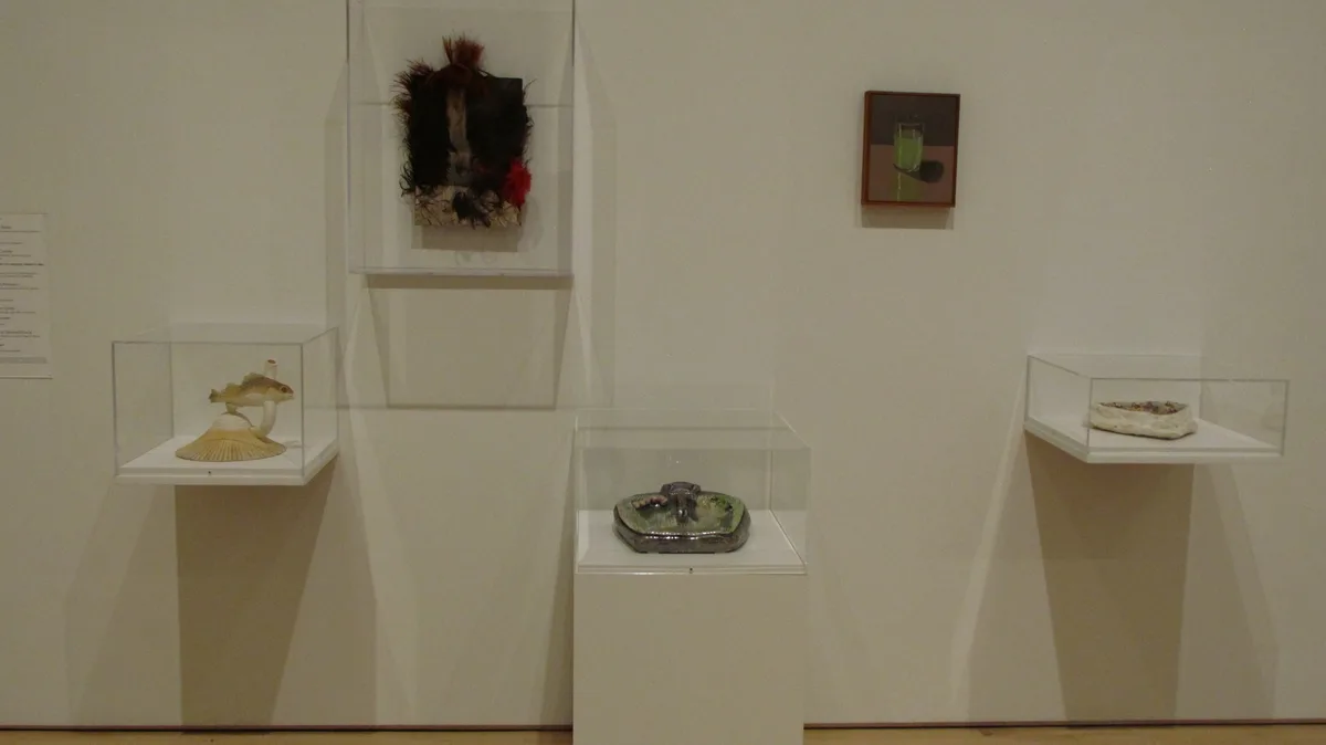 A gallery wall displays several modern art pieces in glass cases and frames, including a fish sculpture on a shell, a…