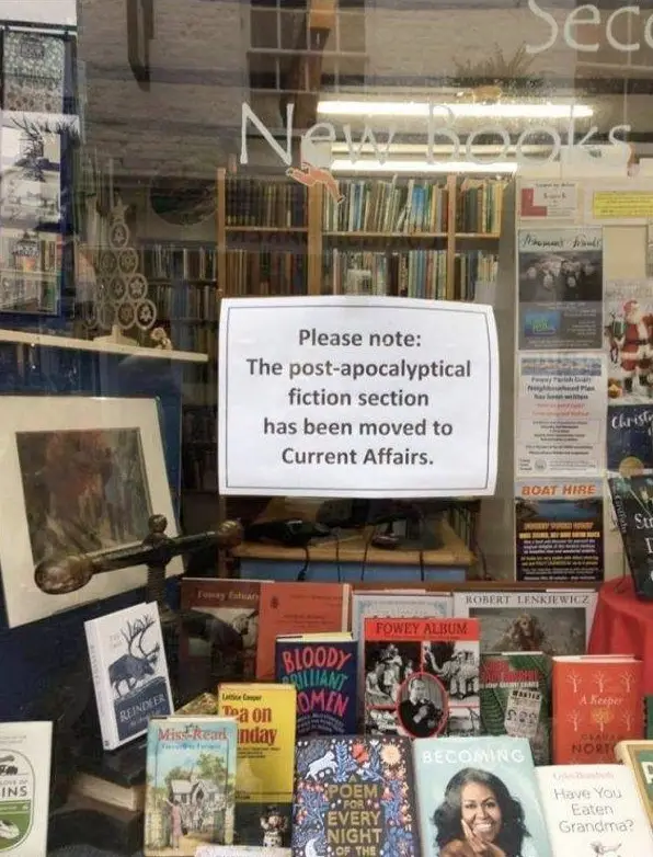 A bookstore window display shows a white sign stating 'Please note: The post-apocalyptic fiction section has been moved to…