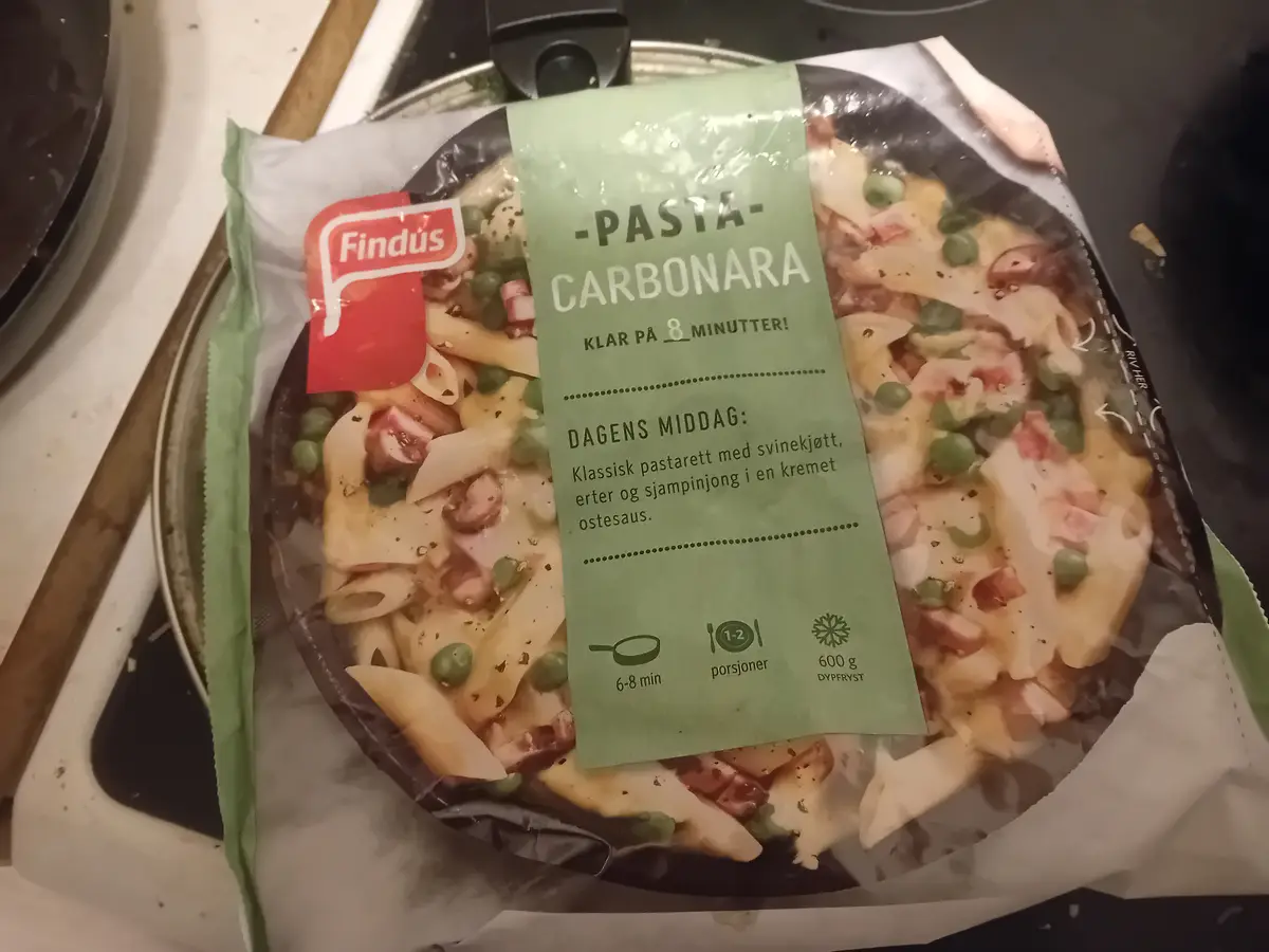A close-up photo of a Findus frozen pasta carbonara meal in its packaging, sitting on a stovetop. The label prominently…