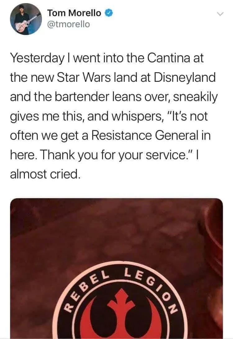 A screenshot of a tweet by Tom Morello shows a close-up photo of a Rebel Legion pin on a dark surface. The pin features the…