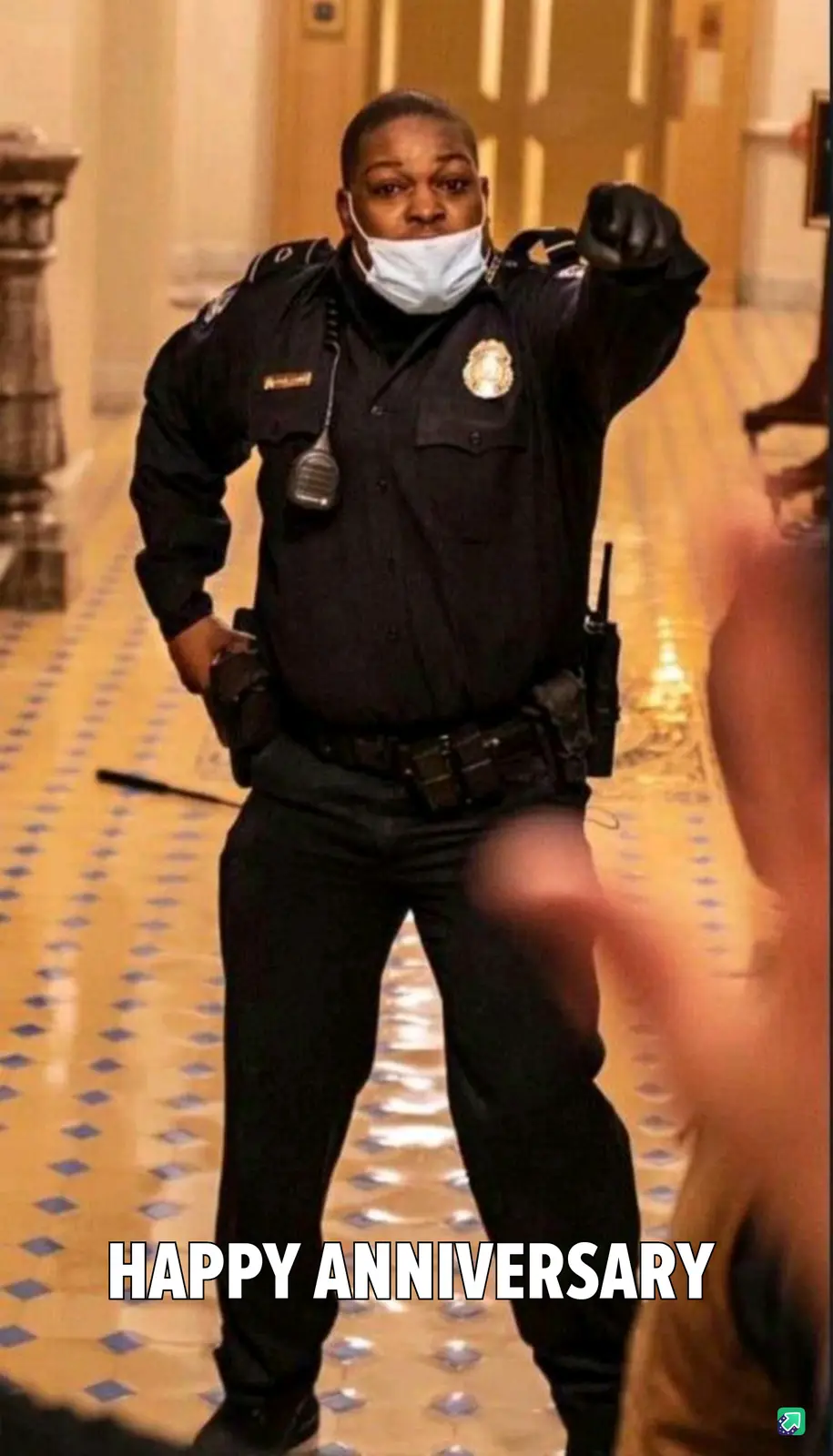 A police officer in uniform, wearing a face mask and holding a baton, stands in a hallway with a blurred figure in front of…