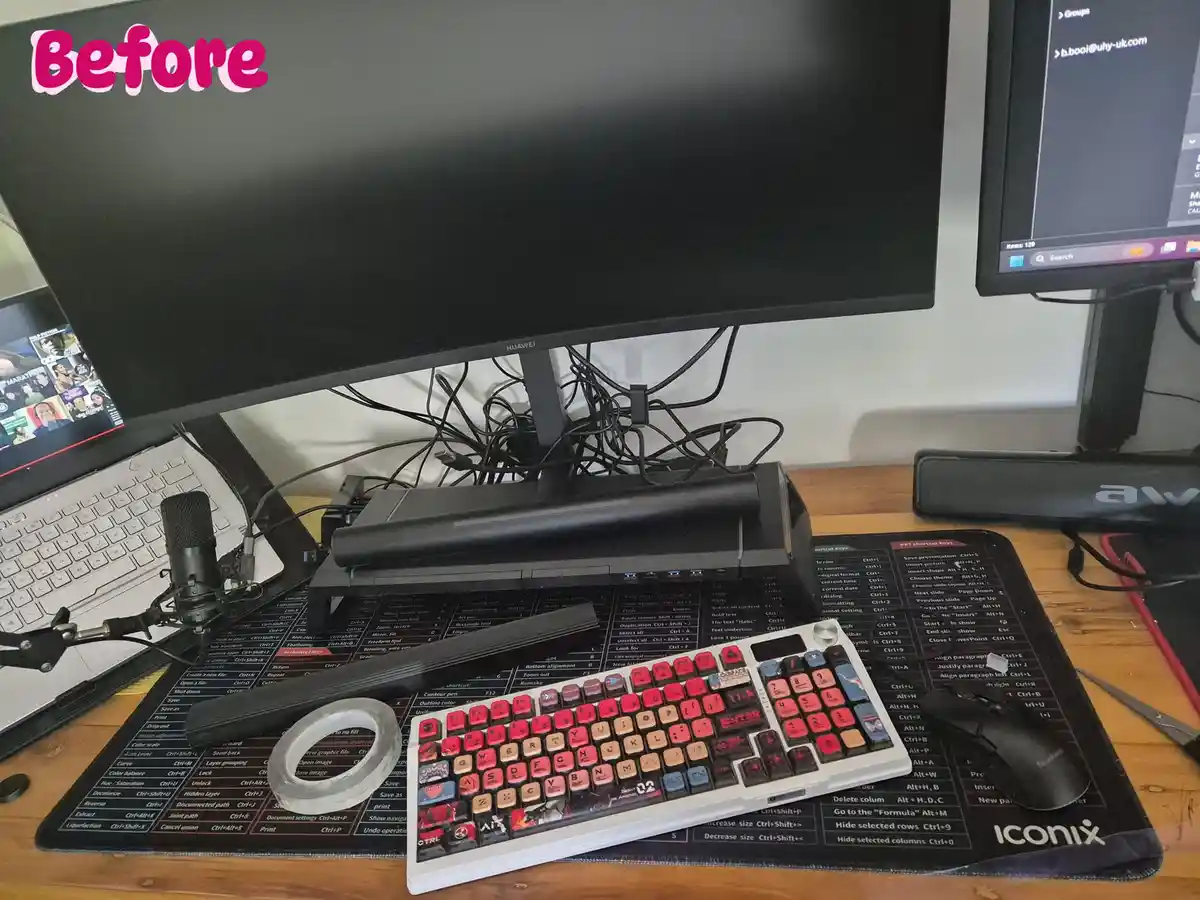 A messy desk setup with a tangled mess of black cables under a large Huawei monitor, a laptop with a microphone, and a…
