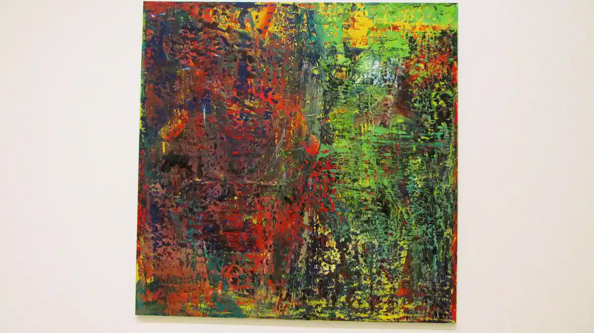 a square abstract painting with chaotic brushstrokes of red, green, yellow, and black hangs on a white wall. The overlaid…