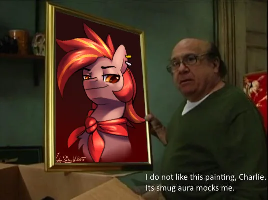 A man in glasses and a green sweater holds up a framed painting of a cartoon pony with fiery orange hair, a red bow, and a…