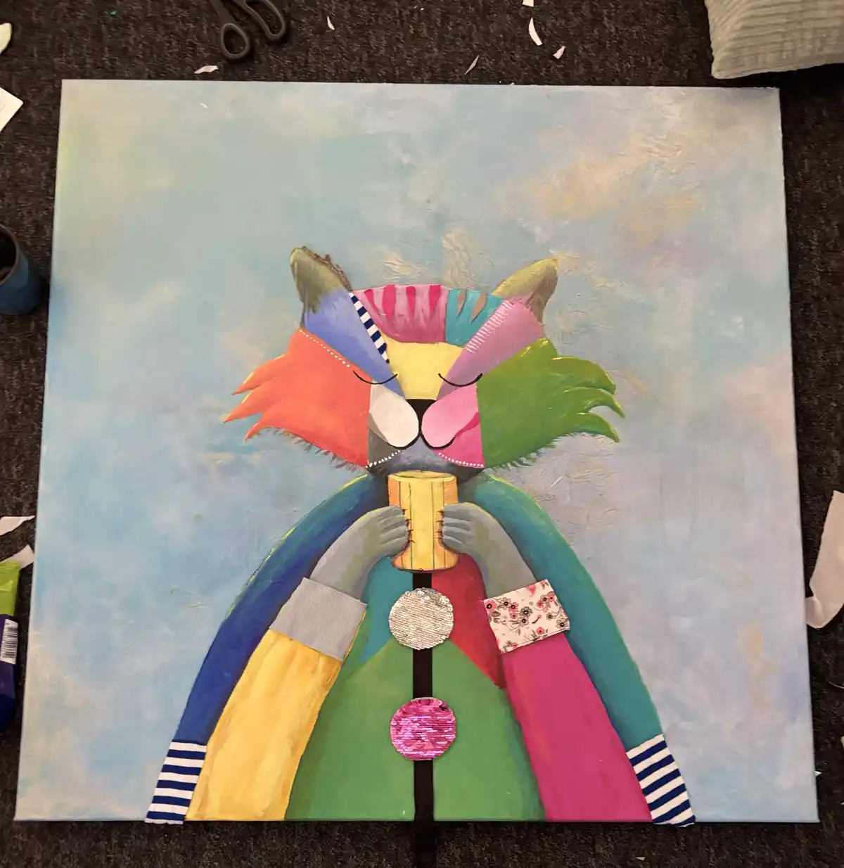 A colorful, patchwork-style painting of a cat wearing a rainbow coat with sequin buttons and holding a mug, set on a dark…