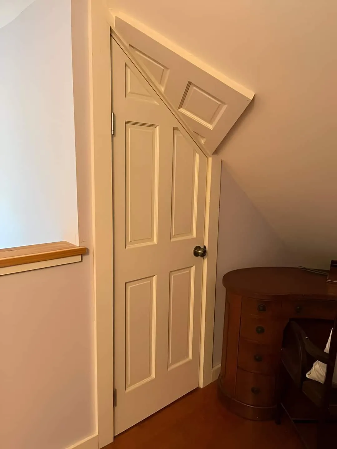 A white six-panel interior door is set in a sloped ceiling, causing its top to be cut off and angled upward. To the right is…