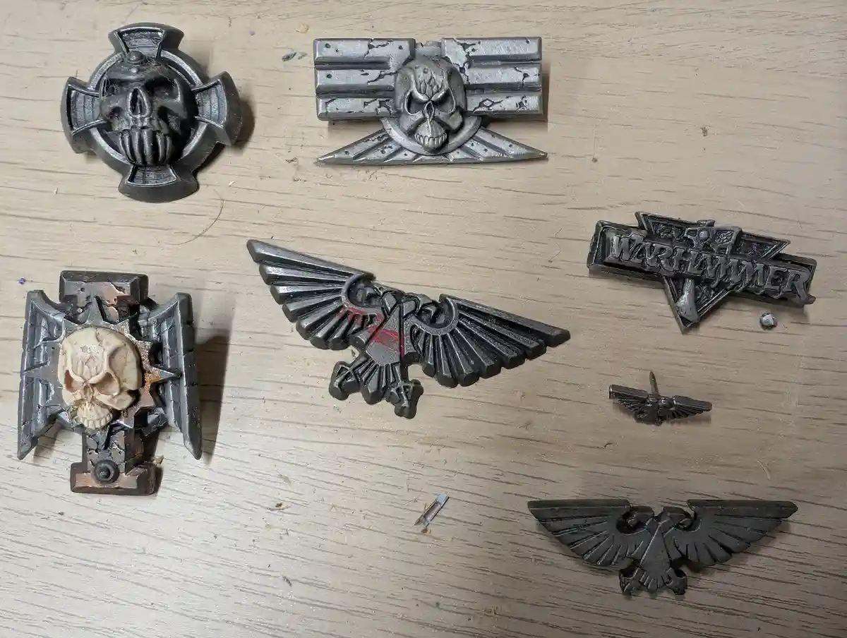 Several Warhammer 40k-themed metal badges and pins, including skull motifs, eagle emblems, and a 'WARHAMMER' logo, are…