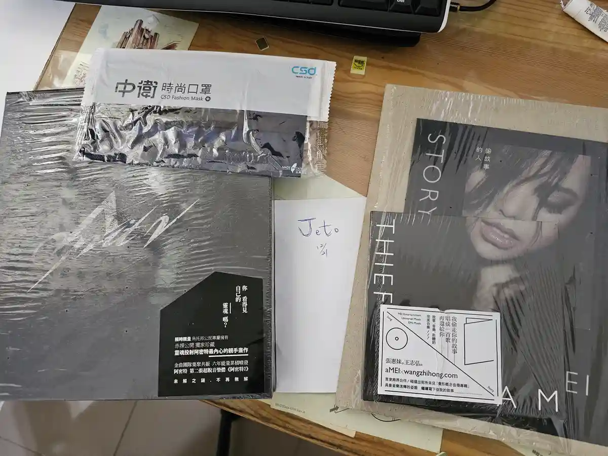 A desk shot shows two sealed music albums by A-Mei, one titled 'The Thief Story' and another 'A-Mei', alongside a packet of…