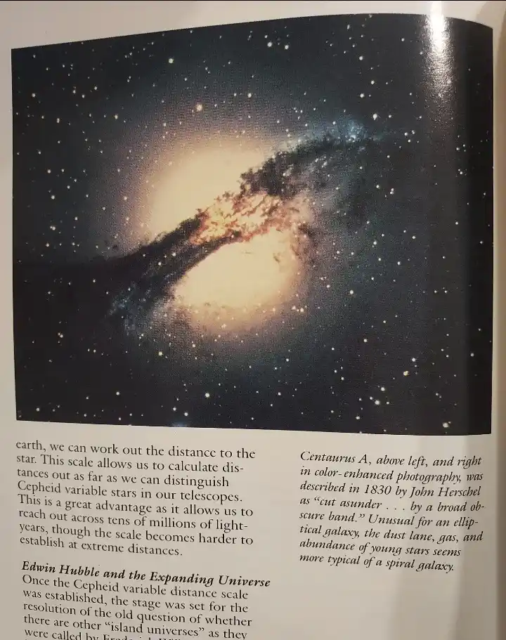 The image shows a page from a book with a color-enhanced photograph of the galaxy Centaurus A, which appears as a large…