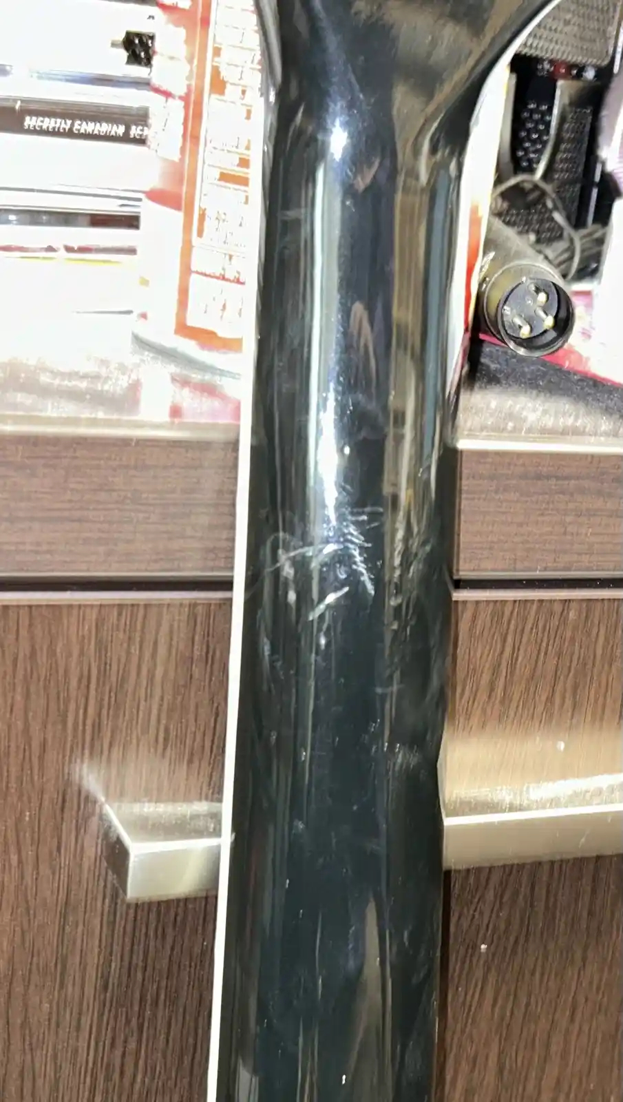A close-up photo shows a shiny black cylindrical object, likely a guitar neck or similar item, with visible scratches and…